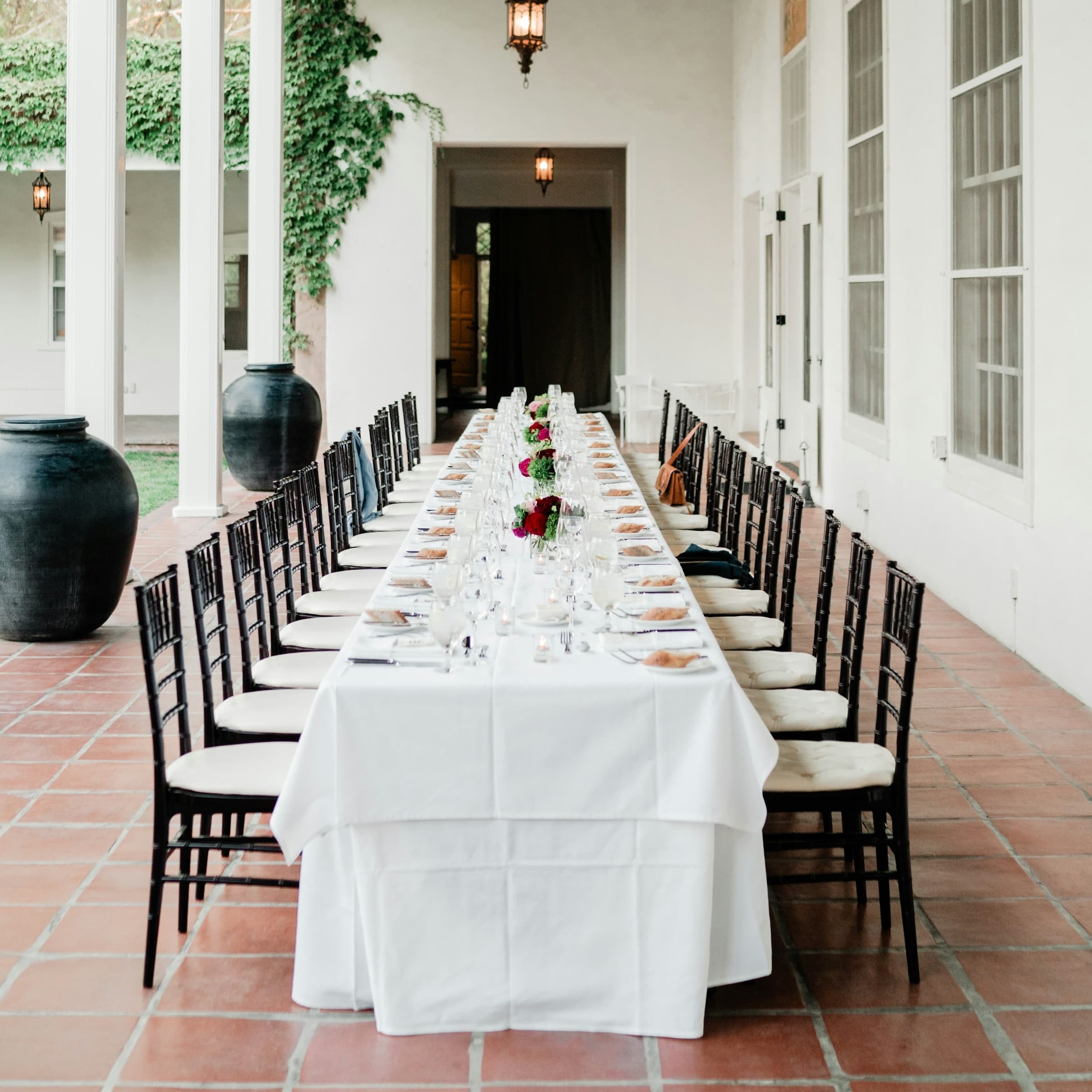 Wedding reception dinner with long table and chairs, setup with tableware and flowers on patio of large manor