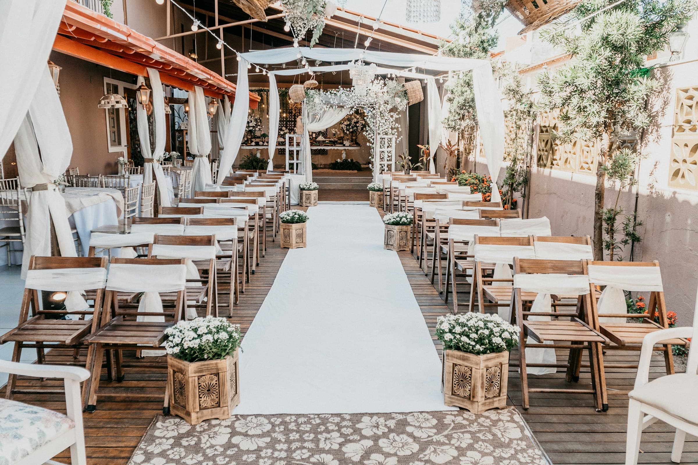 Wedding aisleway with chairs, stringlights, white linens, flowers, on a venue outdoor patio