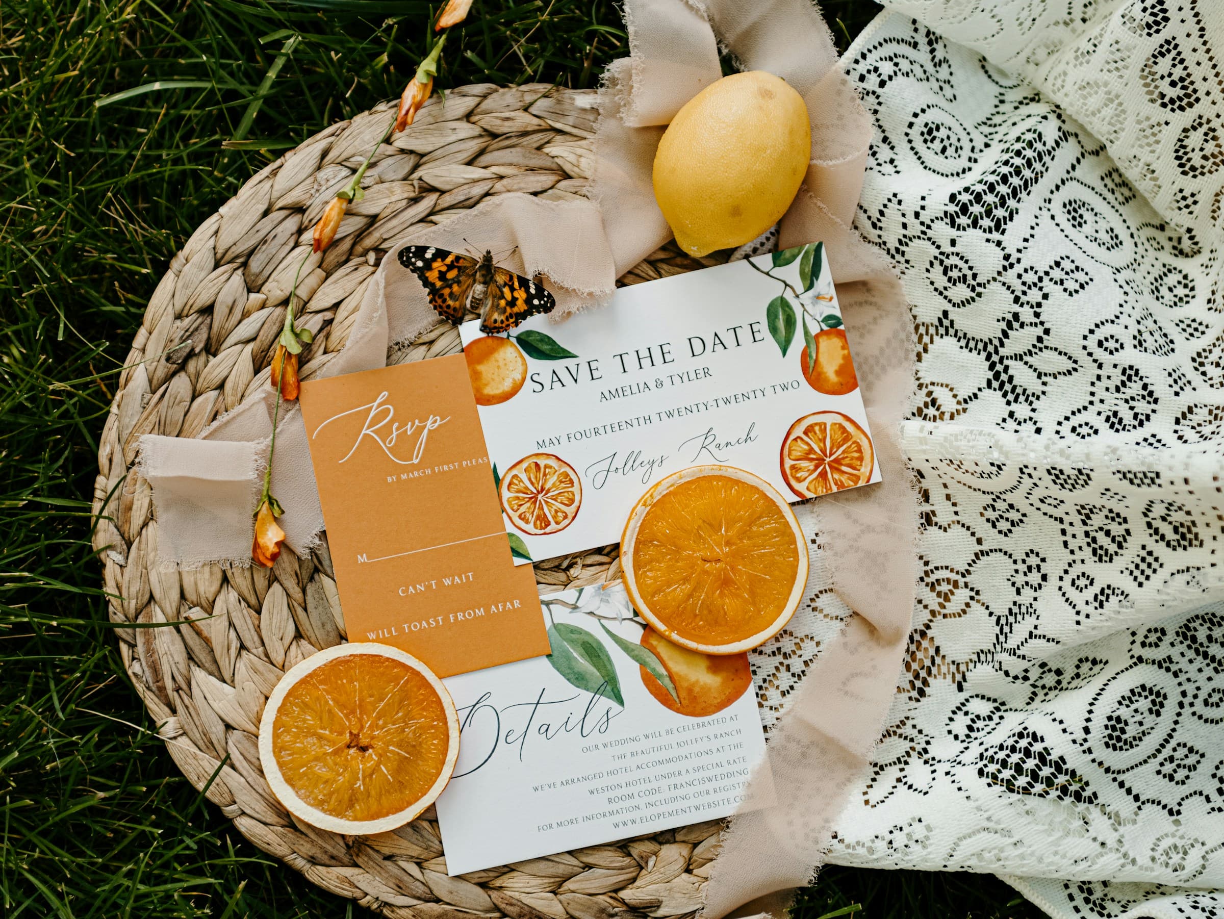 Orange themed wedding invitation, save-the-date, and RSVP card with fresh oranges laid on a linen backdrop