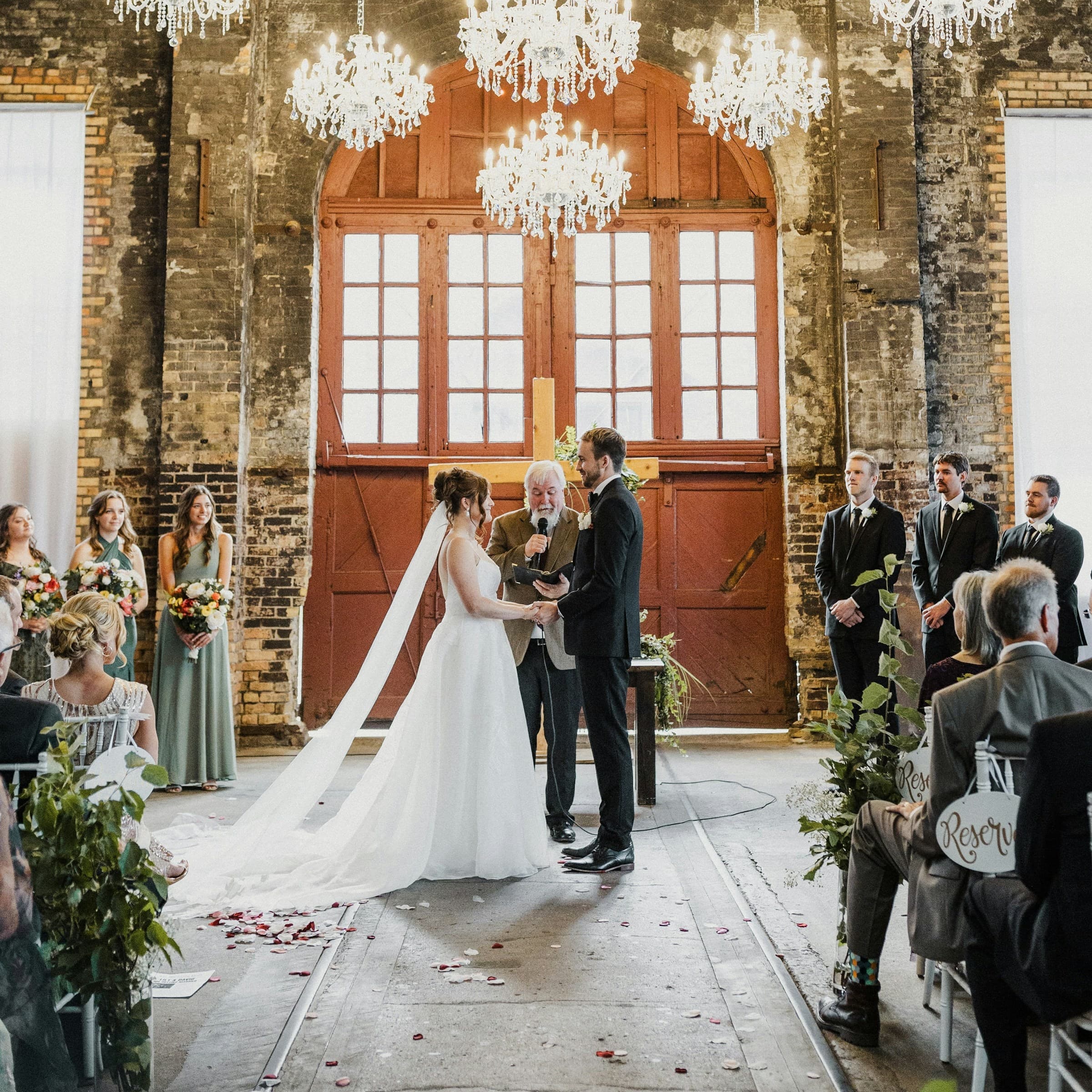 Wedding officiant, bride, and groom in front of guests during wedding ceremony in old rustic barn venue