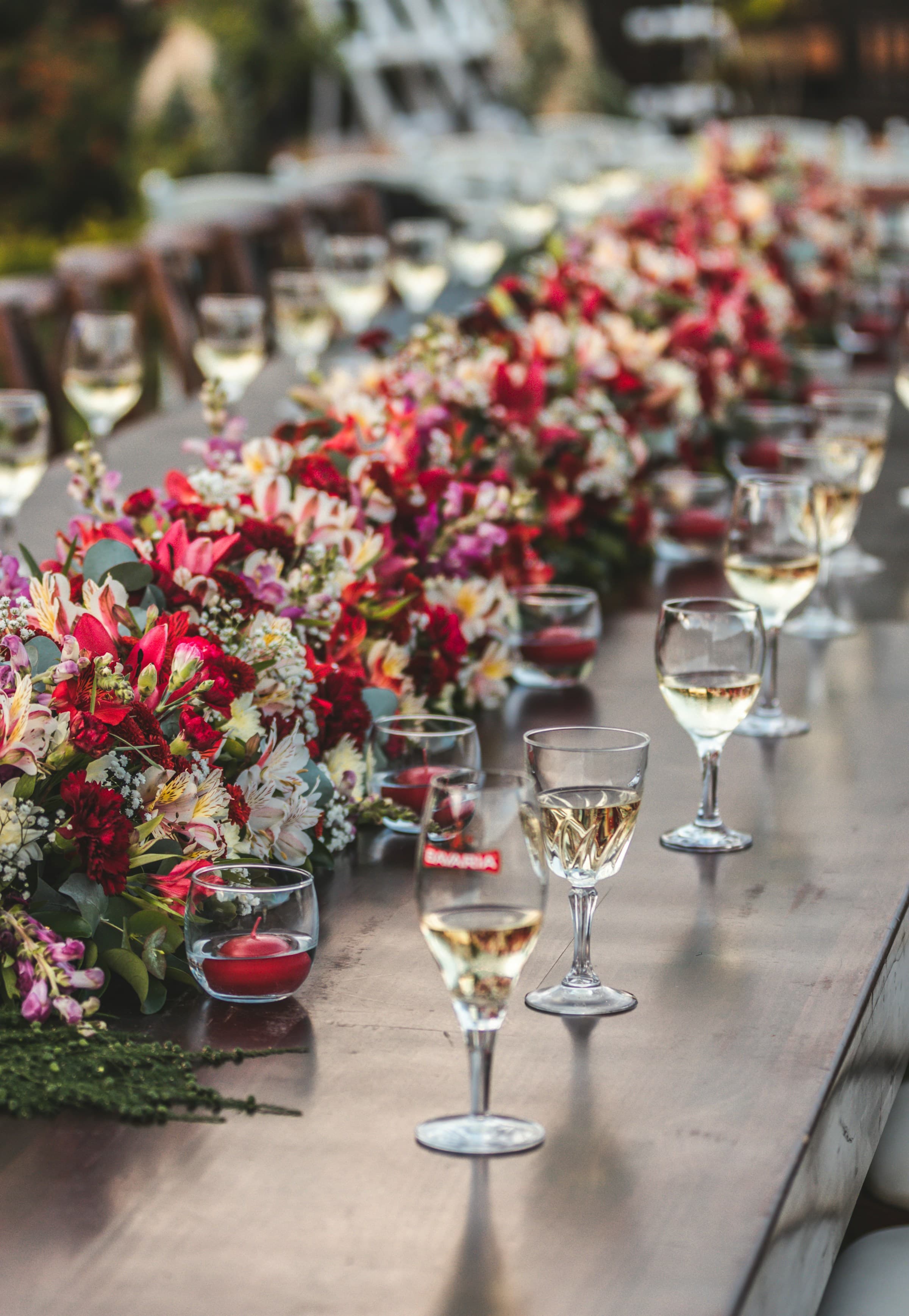 Wedding tables setup with red flowers down the center and wine glasses